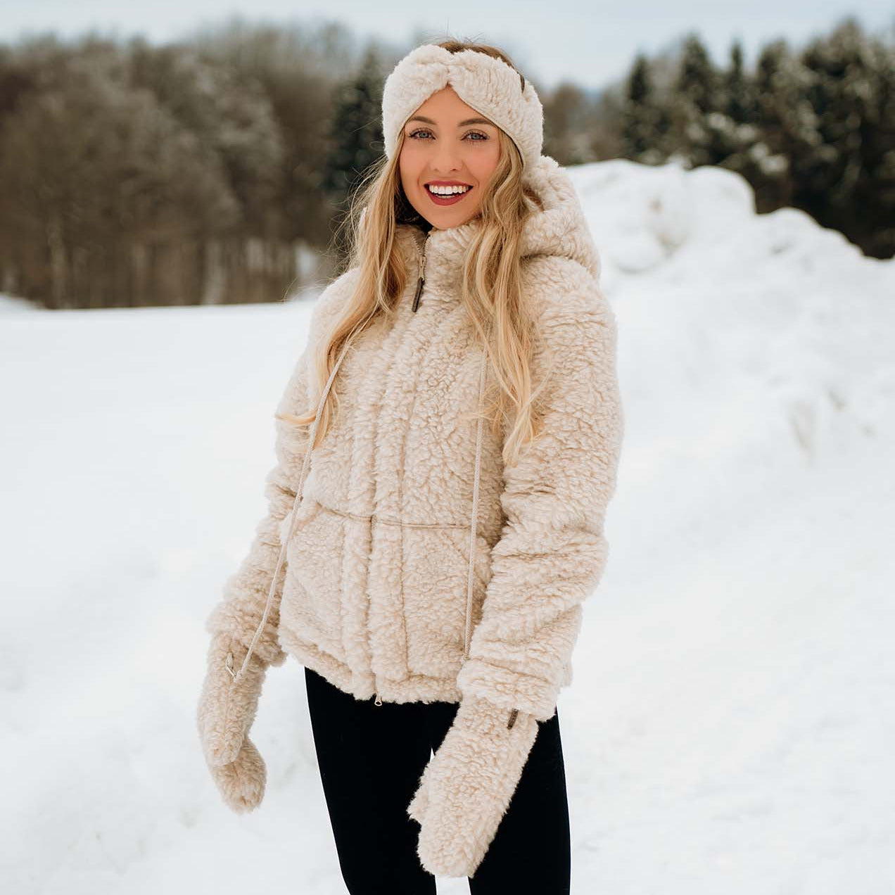 Blond kvinne poserer i snøen iført hvit ulljakke
