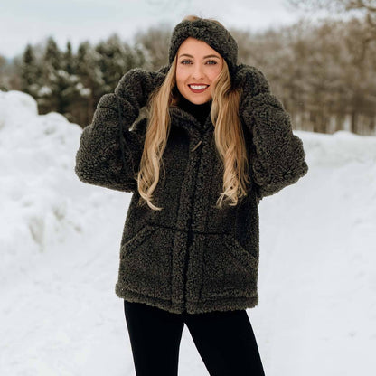 En blond kvinne som poserer i snøen iført en svart grå ulljakke.